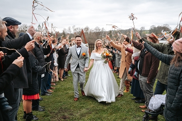 Novomanželé procházejí špalírem se stuhami